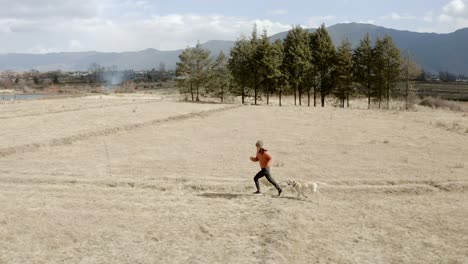 Joven-China-Corriendo-Con-Un-Perro-A-Través-De-Un-Campo-Remoto-En-Las-Montañas-Chinas