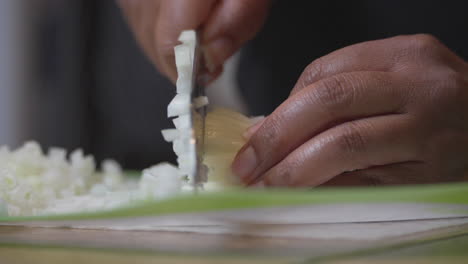 Chopping-an-onion-on-a-cutting-mat-with-a-sharp-knife---isolated-close-up-of-African-American-hands
