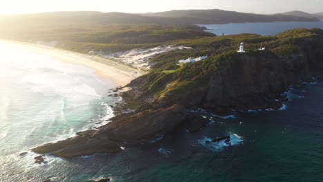 Sugarloaf-Point-Lighthouse-on-Australian-headland-clifftop-at-sunset,-aerial