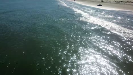 Aerial-drone-view-approaching-fisherman-standing-in-surf-on-beach-on-a-gulf-coast-barrier-island-on-a-sunny-afternoon---South-Padre-Island,-Texas