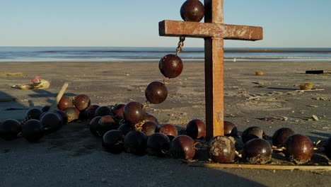 A-cross-wrapped-in-rosary-beads-sits-on-a-beautiful-beach-with-waves-in-the-background