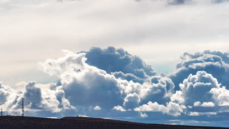 Huge-cumulus-clouds-forming-and-evolving-above-the-silhouette-of-the-Mojave-desert-and-a-cellular-tower---time-lapse