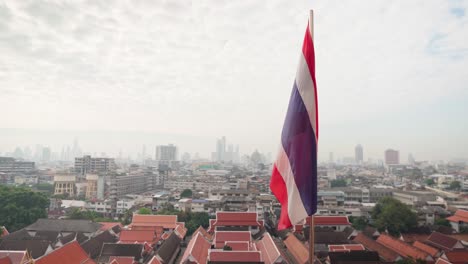 4K-Thailand-Staatsflagge,-Die-Im-Wind-Auf-Der-Spitze-Des-Goldenen-Berges-Wat-Saket-Mit-Bangkok-Im-Hintergrund-Flattert