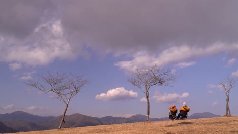 Couple-sitting-in-chair-looking-out-from-top-of-mountain-with-passing-clouds