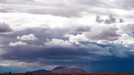 As-torrential-rain-falls-over-the-usually-dry-Mojave-Desert-landscape,-clouds-form,-dissolve-and-evolve-over-the-rugged-mountains---time-lapse