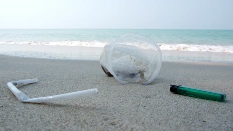Müll-An-Einem-Weißen-Sandstrand,-Ein-Feuerzeug-Und-Ein-Plastikstrohhalm-Und-Eine-Tasse-Lagen-In-Der-Nähe-Des-Ozeans