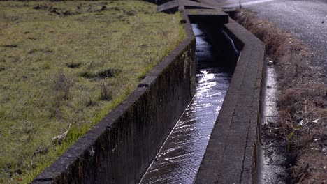 Small-irrigation-river-running-next-to-grass-field-in-rural-setting