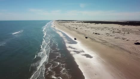 Aerial-drone-view-of-vehicle-driving-on-beach-at-low-tide-on-a-gulf-coast-barrier-island-on-a-sunny-afternoon---South-Padre-Island,-Texas