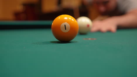 Man-Playing-8-Ball-Pool-Gets-Down-and-Shoots-Solid-Yellow-One-Ball-into-Pocket-Past-Camera-using-Draw-or-Backspin-and-Wooden-Cue-Stick-on-a-Brunswick-Table-with-Green-Felt,-Playing-Billiard-Bar-Games