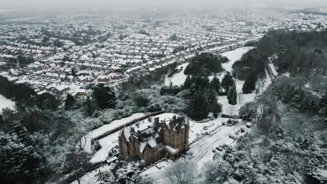 Aerial-view-from-behind-Belfast-Castle-surrounded-by-snow,-tilt-up-reveal