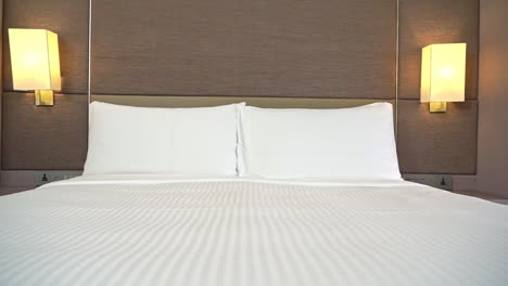 Langsames-Gleiten-Durch-Das-Hotelzimmer-Mit-Gemachtem-Bett-Mit-Zwei-Weißen-Kissen-Und-Gelben-Wandleuchten