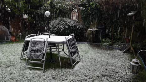 Heavy-wintertime-snow-falling-on-disused-garden-table-and-chairs-in-cold-suburban-residence
