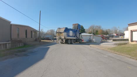 Garbage-truck-lifting-and-emptying-a-trash-dumpster-then-leaves-the-alley