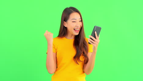 Young-brunette-woman-using-her-mobile-phone-isolated-on-a-green-screen-then-surprised-checking-something-and-starts-to-celebrate-as-if-she-won-a-lottery
