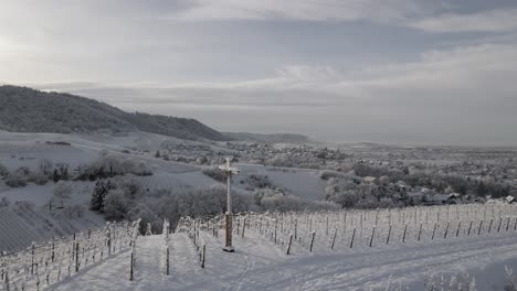 Drone-Orbiting-At-Cross-Situated-On-Snowy-Vineyard-With-Trellis-Near-Zell-Weierbach-In-Offenburg,-Germany