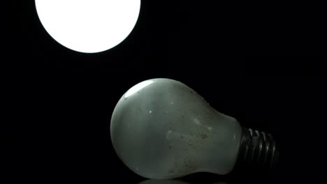Old-incandescent-lamp-and-new-lighten-neon-bulb-shaking-on-black-background,-energy-concept