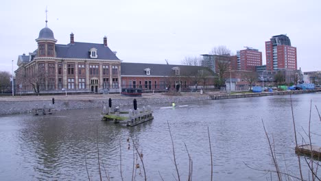 Two-rowers-rowing-along-Utrecht's-canal-on-a-cloudy-day-in-the-Netherlands,-with-a-traditional-brick-building-in-the-background