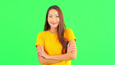 A-pretty-young-woman-against-a-green-background-smiles-as-she-crosses-her-arm-in-front-of-her