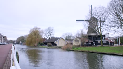 Wideangle-clip-along-Utrecht-canal-on-a-bright-cloudy-day,-showing-peaceful-flowing-water-and-traditional-windmill,-and-a-bridge-in-the-background