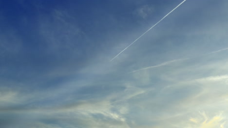 A-Flying-Airplane-Leaves-Contrails-In-A-Beautiful-Blue-Sky-With-Clouds-During-The-Day