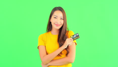 Aufgeregte-Junge-Thailändische-Frau-In-Lässigem-Outfit,-Die-Eine-Kreditkarte-In-Der-Hand-Hält-Und-Auf-Grünem-Studiohintergrund-Lächelt