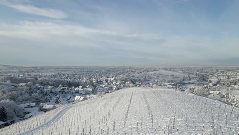 Drone-Flying-Above-Snowy-Vineyard-Hill-With-Cross-Standing-On-Top-In-Offenburg,-Germany