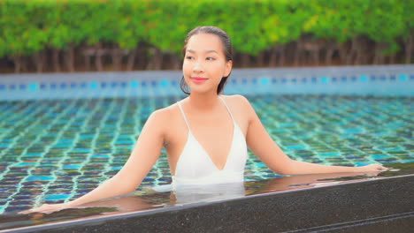 Front-view-of-Smiling-happy-Asian-lady-in-a-swimming-pool-wearing-a-white-bikini