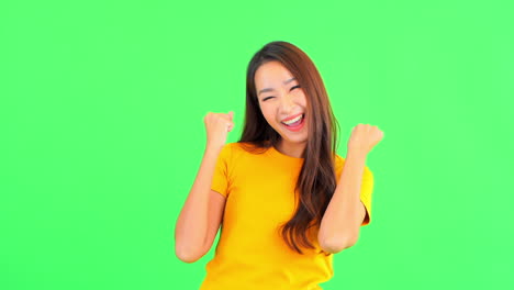 Young-beautiful-model-isolated-on-a-green-screen-expressing-her-positive-mood-by-cheering,-smiling-and-keeping-het-fist-tight-looking-at-the-camera