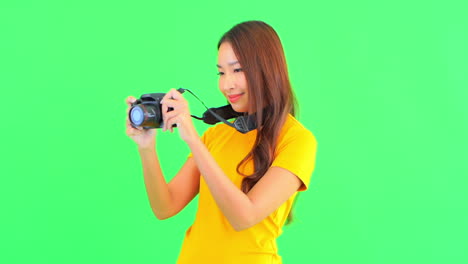 A-pretty-young-woman,-against-a-solid-background,-holds-her-camera-out-in-front-of-her-to-get-a-steady-panorama