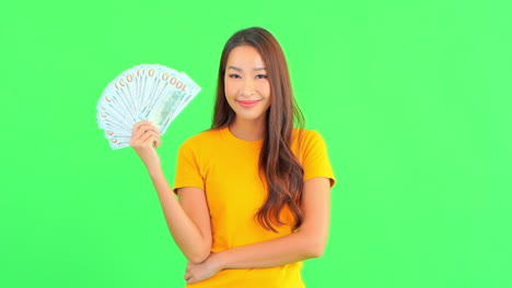 Young-lady-holding-a-paper-bills-in-her-hand-and-pointing-at-it-with-a-smile-on-her-face-and-positive-energy,-isolated-on-a-green-screen