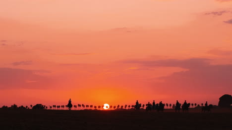 Silhouette-of-several-people-riding-horses-during-beautiful-orange-colored-sunset-in-background