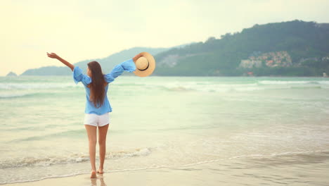Slow-motion-shot-of-a-female-tourist-walking-on-a-wet-sand-,-with-waves-coming-from-the-ocean,-rising-her-arms-in-the-sky