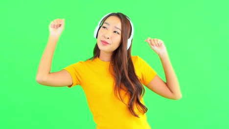 A-pretty-young-woman,-against-a-solid-green-background,-dances-to-the-music-in-her-headphones