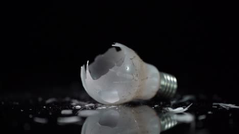 Incandescent-tungsten-light-bulb-of-dusty-lamp-broken-on-glass-pieces-on-black-background