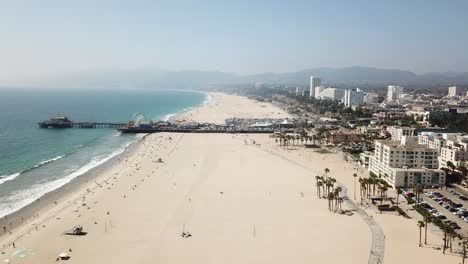 Golden-sandy-beachfront-Los-Angeles-California-coastline-aerial-view-heading-towards-pier