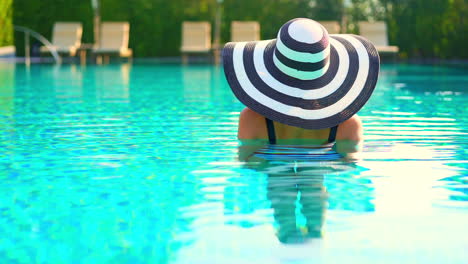 Back-of-Female-With-Summer-Hat-and-a-Swimsuit-Standing-in-Swimming-Pool-on-Sunny-Day,-Full-Frame