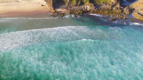 Aerial-shot-of-turquoise-waves-breaking-on-rocky-coastal-beach