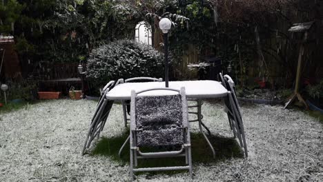 Heavy-wintertime-snowflakes-falling-on-disused-garden-table-and-chairs-in-cold-suburban-residence
