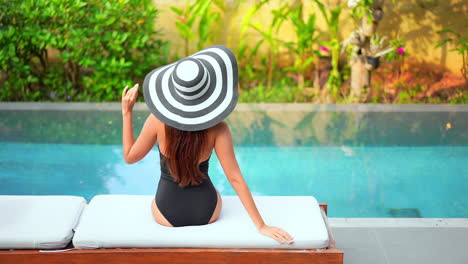 Glamour-Female-in-Swimsuit-and-Big-Summer-Hat-by-Pool-on-a-Tropical-Destination