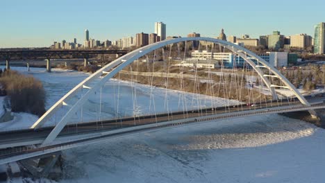 aerial-hold-overlooking-the-white-modern-tied-arch-Walter-Dale-futuristic-overpass-seperating-the-Capital-City-of-Edmonton-over-the-icy-snow-covered-North-Saskatchewan-River-sunny-winter-afternoon-1-2