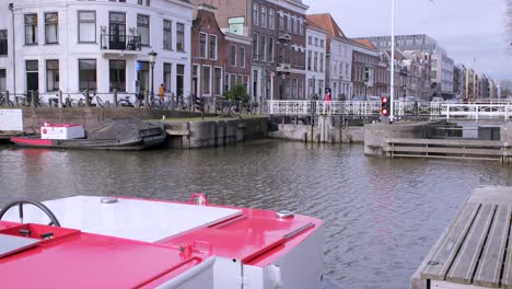 Wideangle-view-of-Utrecht-Canal-showing-a-red-canal-boat-and-people-walking-over-a-canal-lock,-with-historic-buildings-lining-the-canal-and-a-flagpole-in-the-background