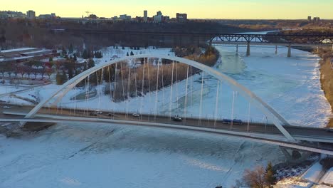 Sunny-Aerial-Fly-over-white-walter-dale-modern-bridge-over-ice-covered-North-Saskatchewan-River-with-the-Low-Level-Vintage-crossing-up-ahead-surrounded-by-Kinsmen-and-Victoria-Park-in-Edmonton-CA-1-4