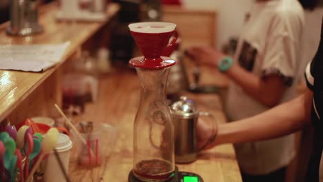 Drops-of-freshly-made-coffee-drip-into-a-glass-jar-on-a-wooden-table
