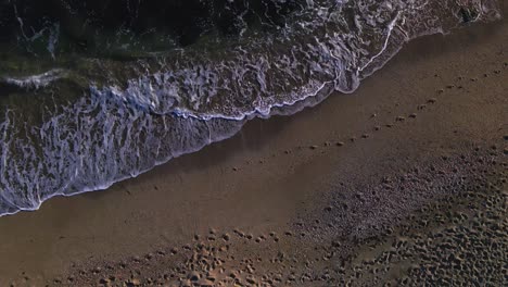 Aerial-view-of-waves-at-the-beach,-moving-closer-to-the-ground-and-tilting-up-into-the-horizon