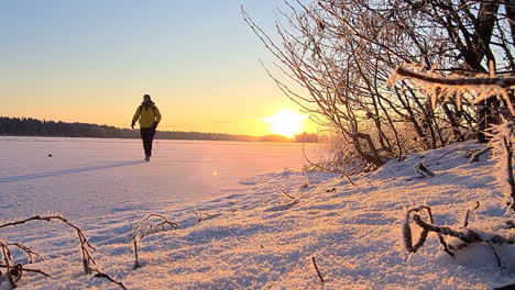 Person-is-walking-on-frozen-lake-in-morning-sunshine-in-beautiful-orange-teal