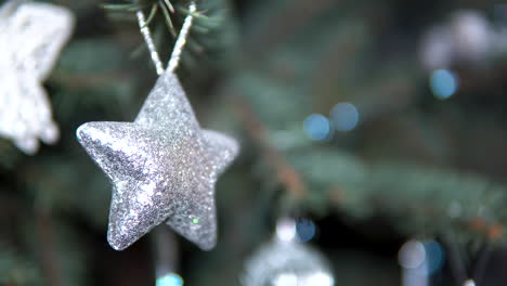 Glitzerndes-Silbernes-Sterndekor,-Das-Am-Weihnachtsbaum-Mit-Verschwommenem-Hintergrund-Aufgehängt-Wurde