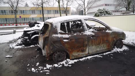 Burnt-out-car-arson-vandalism-on-city-street,-vehicle-covered-in-snow