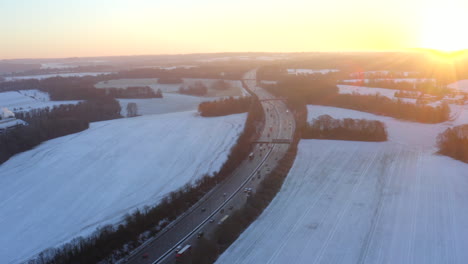 Drone-aerial-footage-of-motorway-surrounded-by-snow-in-fields-with-cars-driving-along-the-M25-in-the-morning-for-sunrise