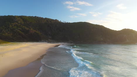 Australia-sandy-beach-on-summer-day,-aerial-shot-over-waves-crashing-on-shore