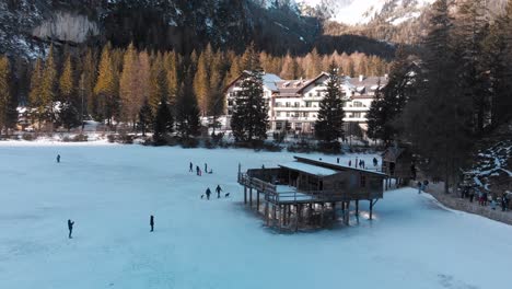 Slow-aerial-pan-of-people-walking-near-an-old-wooden-structure-over-a-frozen-Lake-Braies-in-Italy